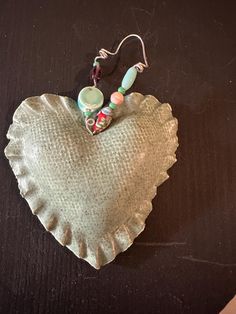 a heart shaped glass ornament with beads hanging from it's side on a table