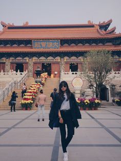 a woman standing in front of a building with stairs and flowers on the ground next to her