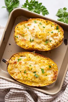 two baked potatoes with cheese and parsley in a baking dish on a white surface