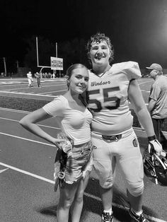 two people standing on a football field posing for the camera with their arms around each other