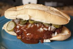 a chili cheese dog with pickles and onions on a blue plate, ready to be eaten