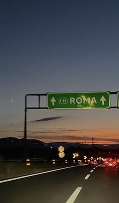 a street sign that reads roma above the highway at night with cars passing by in the foreground