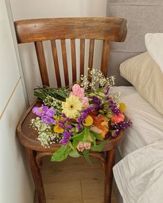 a wooden chair sitting next to a bed with flowers on it's back end