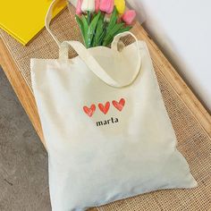 a white bag with flowers in it sitting on a table next to a yellow vase