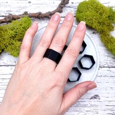 a woman's hand with a black ring on top of a white plate next to some moss