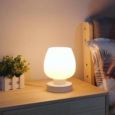 a white lamp sitting on top of a wooden table next to a plant in a vase