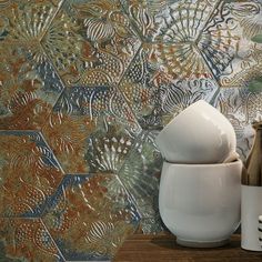 two white vases sitting next to each other on top of a wooden table in front of a patterned wall