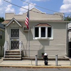 an american flag is flying in front of a small white house with stairs and a fire hydrant