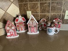 five gingerbread houses are lined up on the counter in front of a tile backsplash