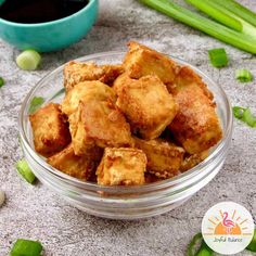 a bowl filled with fried tofu next to green onions