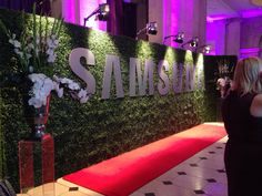 a woman standing in front of a green wall with the words samsung on it and flowers