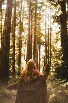 a woman is walking through the woods with her back to the camera and arms outstretched