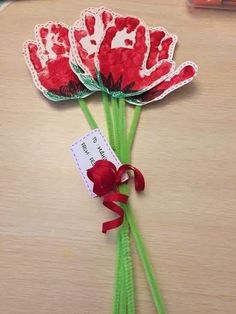 two red flowers with green stems and a tag tied to them on a wooden table