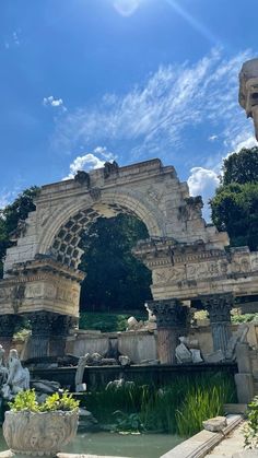 an arch in the middle of a garden with statues on either side and water below