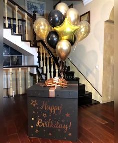 a black box with gold and silver balloons in it sitting on the floor next to stairs