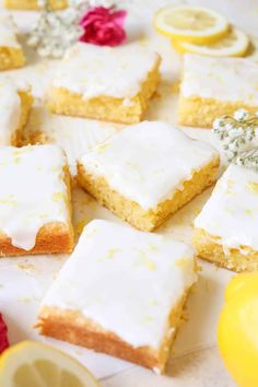 lemon bars with white frosting and flowers on the table next to sliced lemons