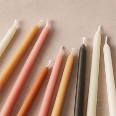 five candles lined up in different colors on a white tablecloth with one candle lit