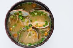 a bowl filled with soup and clams on top of a white countertop next to a wooden spoon