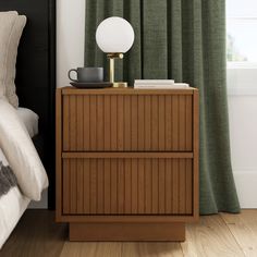 a nightstand with a lamp on top of it in front of a green drapes