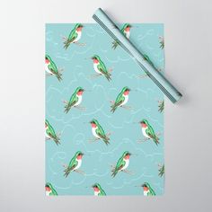 a blue wrapping paper with green and red birds on it, next to a pencil