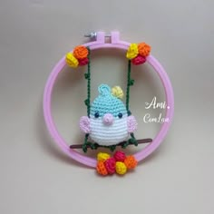 a small crocheted bird hanging from a pink hoop with flowers on it's side