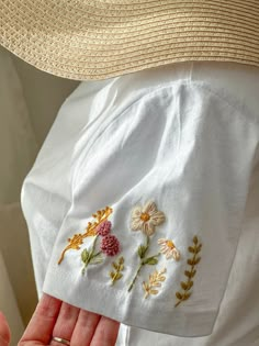 a person wearing a hat and white shirt with embroidered flowers on the back of it