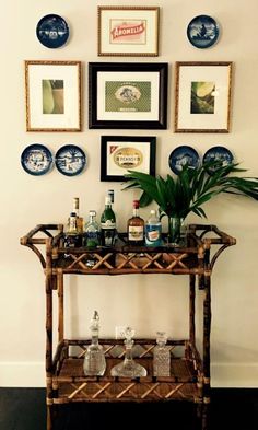 a bar cart with bottles and glasses on it in front of several framed pictures above