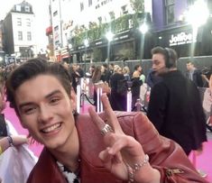 a young man making the peace sign on the red carpet at an awards event with people in the background