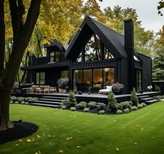 a large black house sitting in the middle of a lush green field with lots of trees