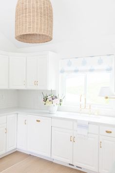 a kitchen with white cabinets and wooden flooring is pictured in this image, the light fixture hangs over the counter