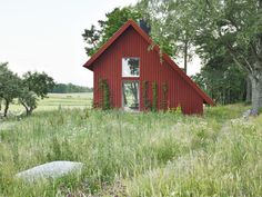 a red house sitting in the middle of a lush green field next to some trees