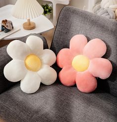 two flower shaped pillows sitting on top of a gray chair next to a white lamp