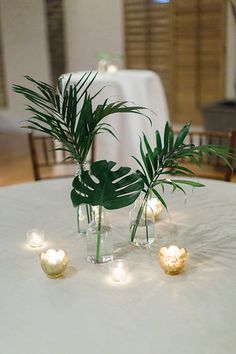 the table is set with candles and greenery in vases on top of it