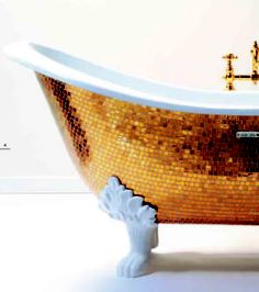 an old fashioned bathtub with gold mosaic tiles on the side and feet, in front of a white wall