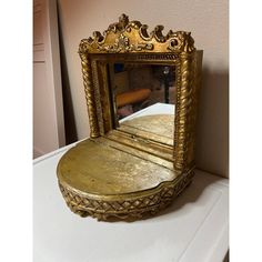 an ornate gold mirror sitting on top of a white counter next to a pink wall