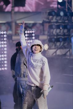 a man standing on top of a stage with his arms in the air while wearing a white sweater and hat