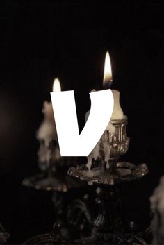 three lit candles sitting on top of a metal stand with the letter v in front of them