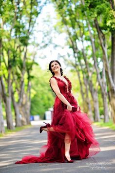 a woman in a red dress is standing on the street with trees and grass behind her