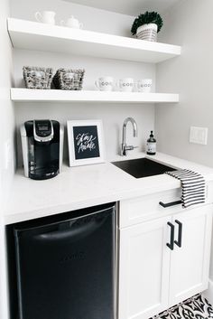 a black and white kitchen with open shelving above the sink, dishwasher and coffee maker