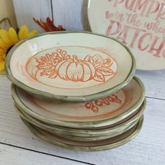 four plates with pumpkins painted on them sitting next to a yellow flower and some other items