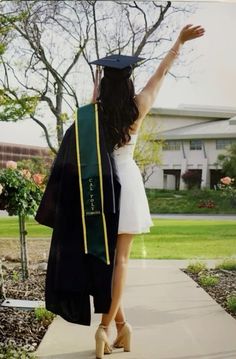 a woman in a graduation gown and cap walking down a sidewalk with her arms up