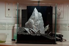 a rock in a glass box on a counter top with a light above it and a bowl next to it