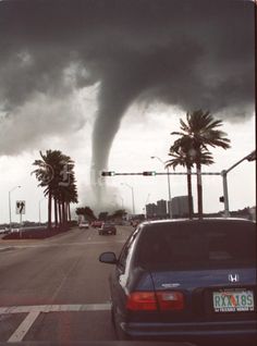 a car parked in front of a very large tornado that is coming out of the sky