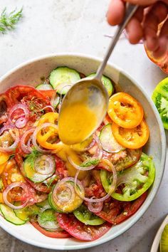 a bowl filled with vegetables and dressing being drizzled over the top by a spoon