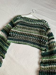 a green and white knitted sweater hanging on a clothes hanger next to a bed