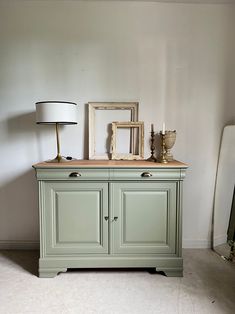 a green cabinet with two pictures on top and a lamp next to it in front of a white wall