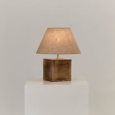 a table lamp sitting on top of a white block with a beige shade over it