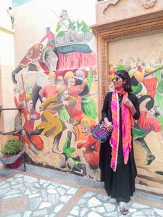 a woman standing in front of a painting on the side of a building with a pink scarf around her neck