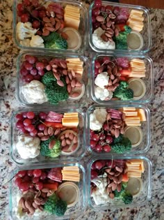 four plastic containers filled with different types of food on top of a marble countertop