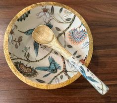 a wooden spoon sitting in a bowl with flowers and birds on it's side